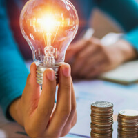 Woman holding lightbulb next to stack of coins